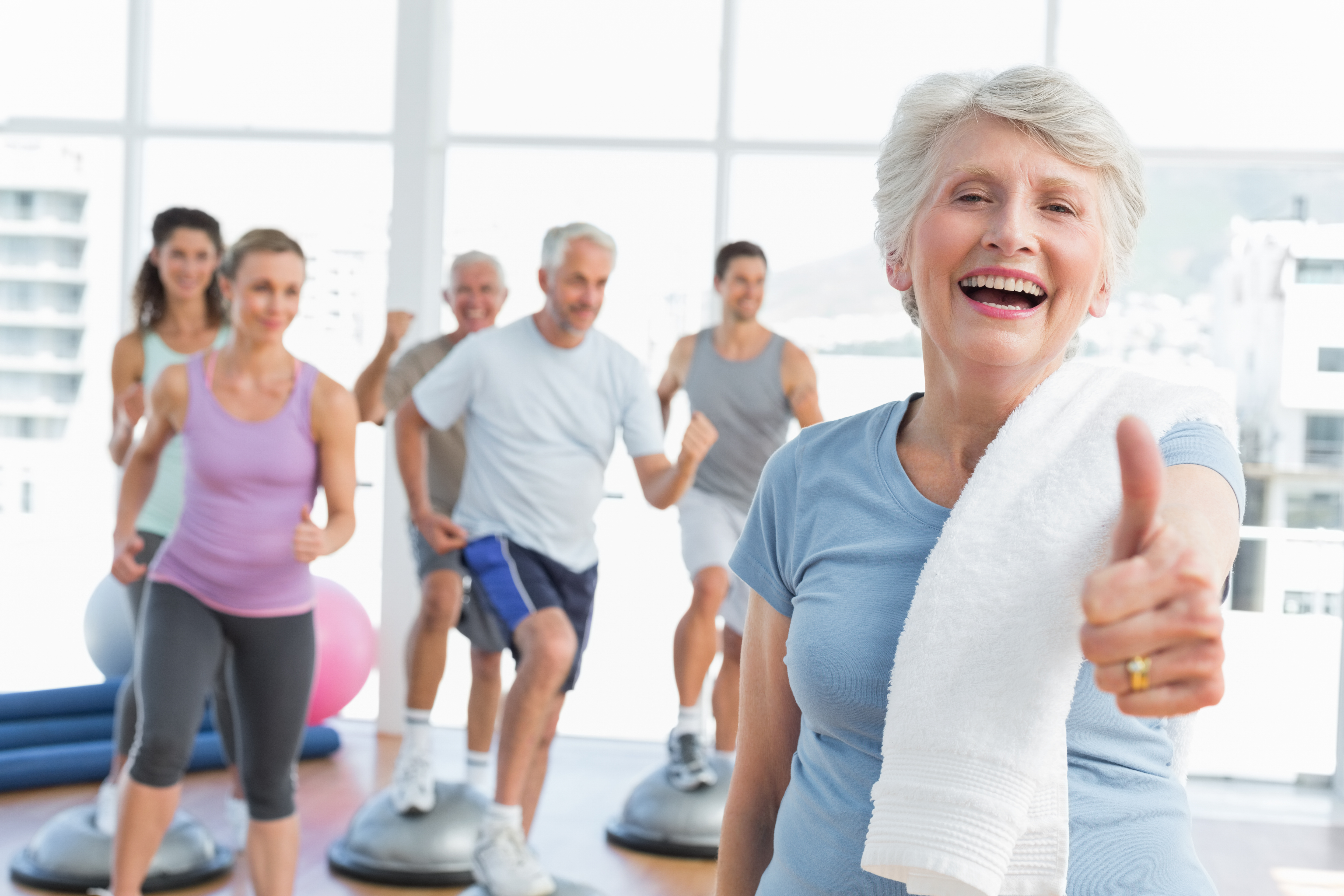 Cheerful senior woman gesturing thumbs up with people exercising